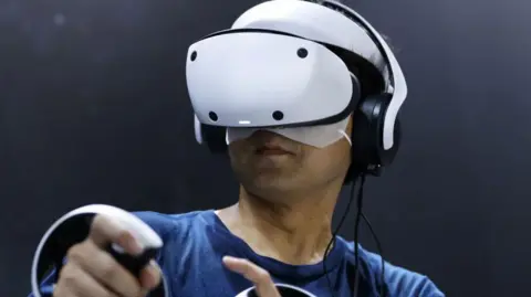 Getty Images A man uses the PlayStation VR 2. It's larger than the other two headsets and is a smooth, curved white shape.